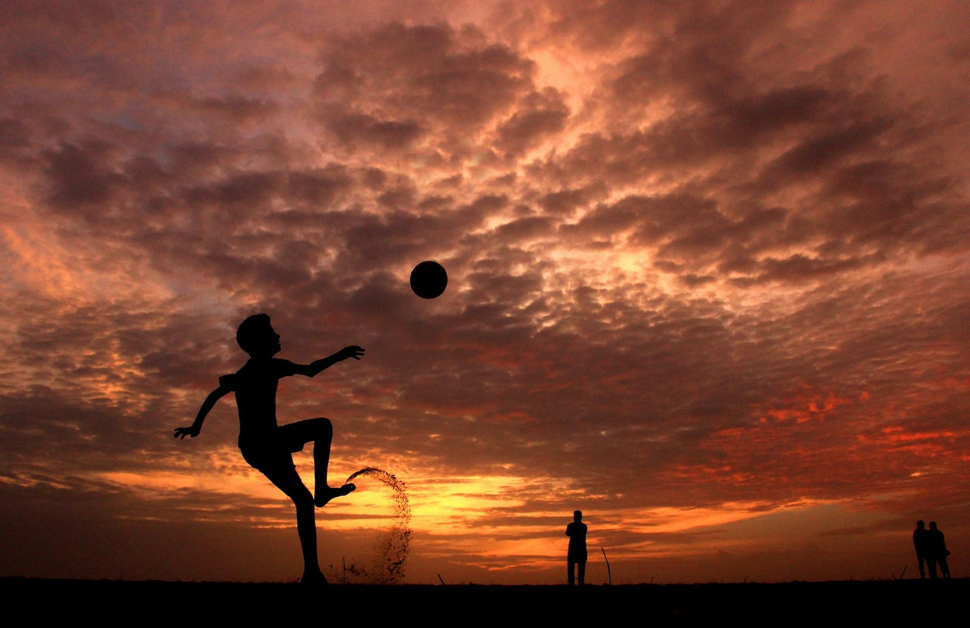 Football player on beach in sunset getting ready for a bicycle kick